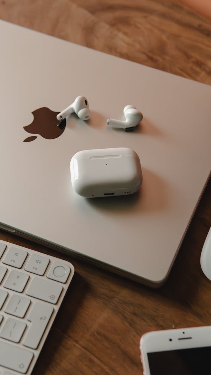 Home MacBook with wireless earphones and keyboard on a wooden desk, a tech-savvy workspace.